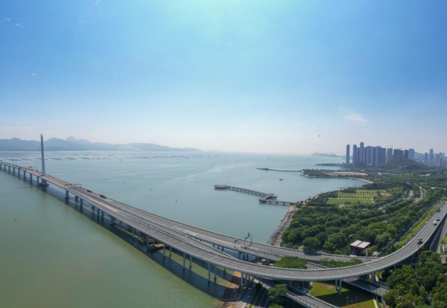 深圳湾大桥是继罗湖、皇岗和沙头角之后深圳第4条跨境通道，全长5545米，设南北两个通航桥，主跨分别为210米和180米。大桥连接深圳蛇口与香港元朗，为中国公路干线网中唯一与香港连接的高速公路大桥，也是广深沿江高速公路的咽喉。广州与香港的距离因该桥建成通车缩短至100千米。大桥深圳侧独塔斜拉桥塔采用向香港侧倾斜的斜塔，与香港侧斜拉桥的桥塔向深圳侧倾斜互相对应，寓意深港两地手牵手走向一起。图为深圳湾大桥。